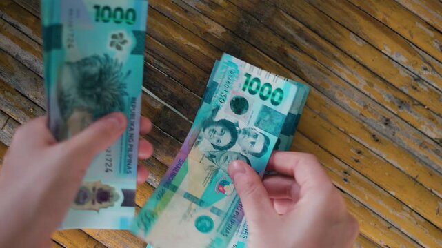 Close-up of a Person Holding and Counting New Philippine 1000 Peso Polymer Banknotes Over a Rustic Wooden Table Surface &ndash; Featuring Hands, Currency Security Details, and Filipino Historical Figures