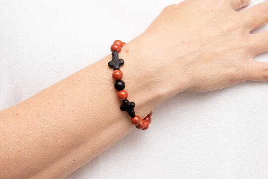 Pulseira de esferas de pedra de cor vermelha com pequenas cruzes de hematita no pulso de uma bra&ccedil;o feminino. 