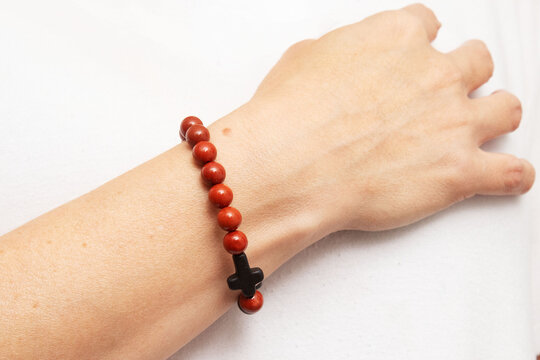 Pulseira de esferas de pedra de cor vermelha com pequenas cruzes de hematita no pulso de uma bra&ccedil;o feminino. 