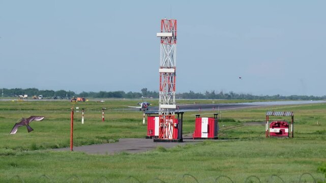 Airport instrument landing system antennas and localizer tower installed along green runway field under clear sky.