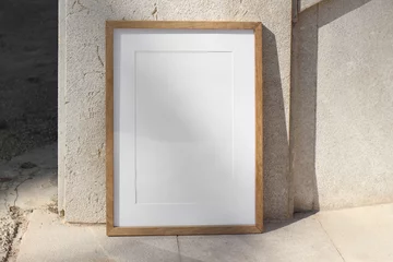  Vertical wooden picture frame leaning against stone wall in sunlight. Textured beige tiles background. Summer outdoor natural, minimal backdrop. Empty poster mockup, branding display. © tabitazn