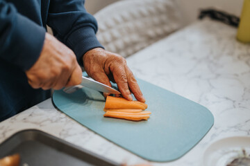 Hands slicing fresh carrots on a cutting board, showcasing food preparation in a kitchen. The...