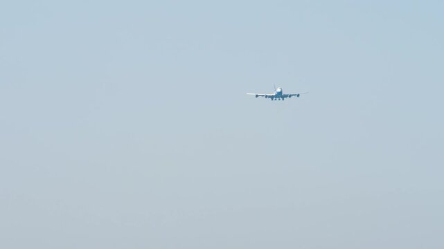 A huge four-engine aircraft with an unrecognizable livery approaching landing, front view long shot. Airplane in blue sky background. Travel concept