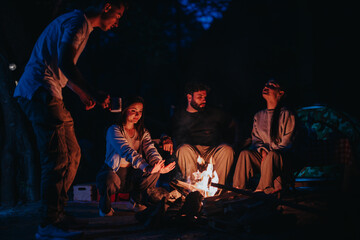 A group of friends relaxing around a campfire in the evening, enjoying warmth and camaraderie in an...
