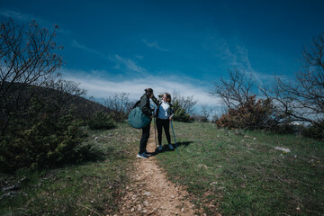 Obraz premium Two people with hiking gear and walking sticks explore a nature trail surrounded by green foliage and a clear blue sky, embracing the outdoor adventure on a sunny day.