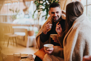 Close-up of a smiling man and woman chatting while enjoying drinks, wrapped in blankets, in a...