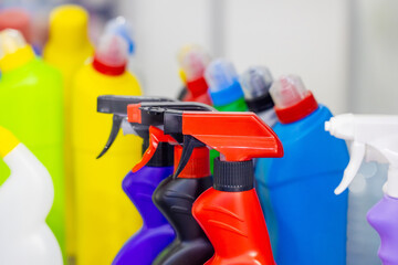 Assorted colorful plastic cleaning product bottles and spray nozzles on a shelf, featuring vibrant...
