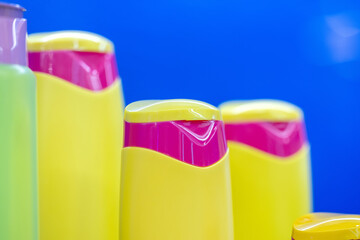 Brightly colored yellow and pink shampoo bottles in a row against a vibrant blue background, showcasing modern packaging design and color contrast, close-up view. Selected focus