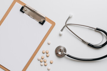 Stethoscope on white desk with clipboard and pills, clean flat lay.