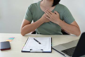 An asian young business woman is holding her pain area and sitting at office desk and suffering...