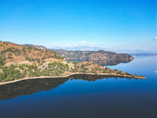 Obraz premium Lush green mountain reflected in clear water. Vibrant natural landscape with rich vegetation and a calm lake or river at the base of the hill.