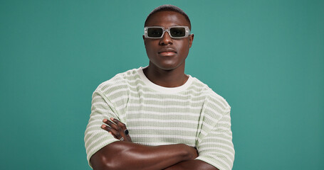 Black man, fashion and sunglasses with arms crossed, style and confidence on green studio...