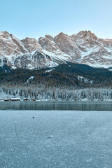 Mesmerizing Twilight Alpine Wonderland: Eibsee Lake Reflects Snow-Capped Zugspitze Mountain Amidst Illuminated Pine Forest Enchanting Winter Landscape Captures Serene Beauty of German Ski Resort at