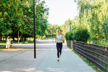 Mature woman wearing sportswear running in a city park during a sunny summer day, enjoying her outdoor training session surrounded by nature and fresh air