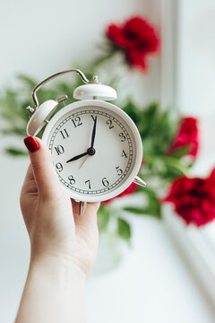 Hand holding white clock with vibrant peonies in background
