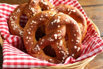 Tasty pretzels with salt in wicker basket on table, closeup