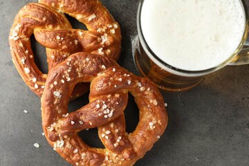 Tasty pretzels and glass of beer on dark textured table, flat lay