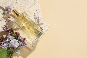 Bottle of perfume and beautiful lilac flowers on pale yellow background, flat lay. Space for text