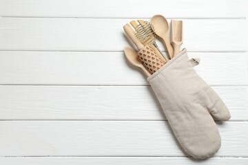 Different kitchen utensils in oven mitten on white wooden table, top view. Space for text