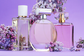 Bottles with perfumes and lilac flowers on purple gradient background, closeup