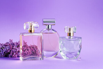 Bottles with perfumes and lilac flowers on purple gradient background, closeup