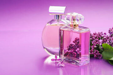 Bottles with perfumes and lilac flowers on mirror surface against color gradient background,...