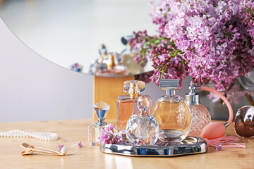 Bottles of perfumes, accessories and lilac flowers on wooden table