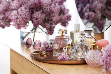 Bottles with perfumes, lilac flowers and accessories on dressing table indoors, closeup
