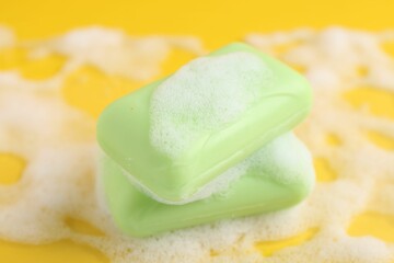 Soap bars with foam on yellow background, closeup