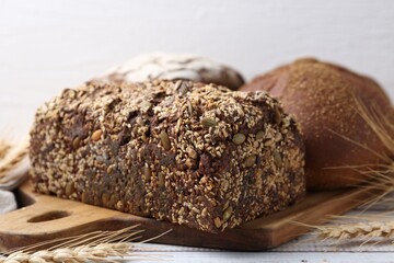 Fresh bread loaves and spikes on white wooden table, closeup
