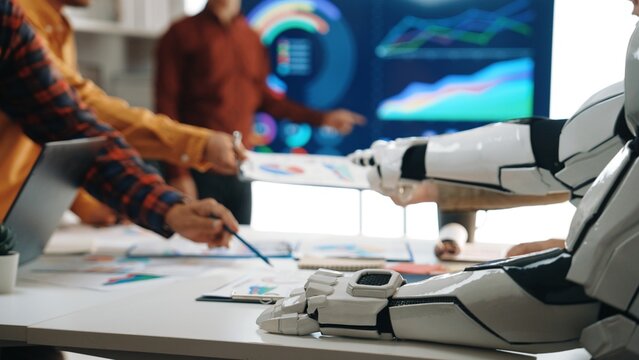 A diverse team engages in a dynamic meeting, showcasing futuristic collaboration with AI while analyzing visual data charts in a modern office environment.Noogenesis - Powered by Adobe