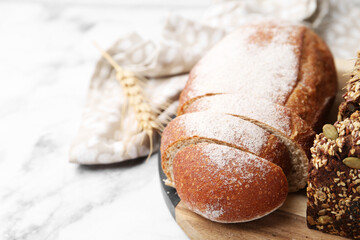 Freshly baked loaves of bread and spikes on white marble table, closeup. Space for text