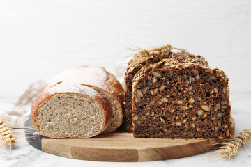 Freshly baked loaves of bread and spikes on white marble table, closeup
