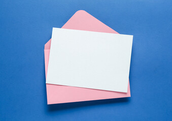 Blank invitation card and envelope on blue background, top view. Space for design