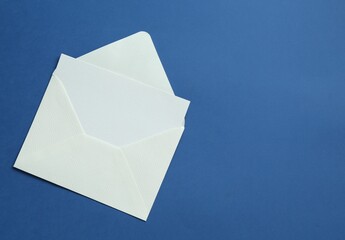 Blank invitation card and envelope on blue background, top view. Space for text