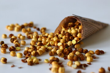 Crispy Roasted Channa chickpeas in a newspaper cone, scattered on white background.