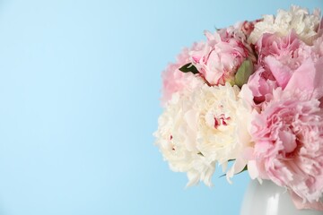Beautiful peonies in vase on light blue background, closeup. Space for text