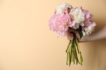 Woman holding bouquet of beautiful peonies on beige background, closeup. Space for text