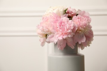 Beautiful peonies in vase near white wall, closeup