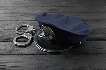 Police cap and handcuffs on black wooden table, closeup