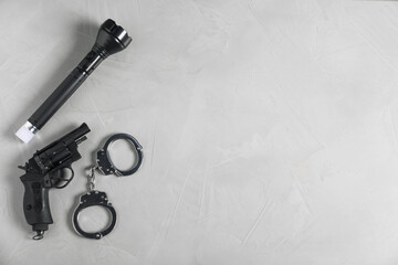 Gun, handcuffs and flashlight on light grey table, flat lay. Space for text