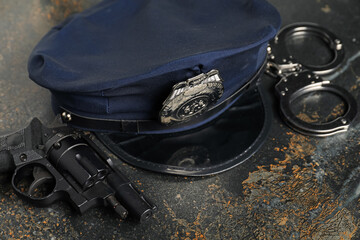 Police cap, handcuffs and gun on dark table, closeup