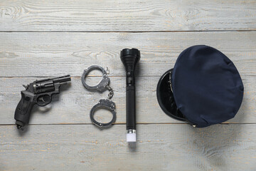 Police cap, flashlight, handcuffs and gun on grey wooden table, flat lay