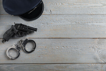 Police cap, gun and handcuffs on grey wooden table, flat lay. Space for text