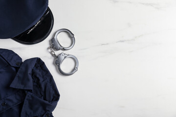 Police uniform and handcuffs on white marble table, flat lay. Space for text