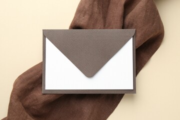 Blank invitation card and envelope on beige background, top view