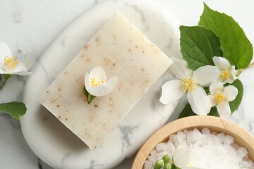 Soap bar, sea salt and jasmine flowers on white marble table, flat lay