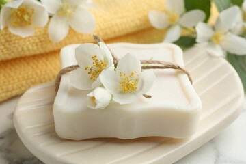 Soap bar and jasmine flowers on white marble table, closeup