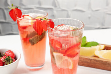 Refreshing drink with strawberries, lemon and ice on white table against grey textured background, closeup