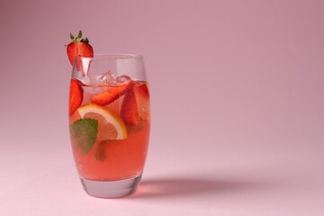 Refreshing drink with strawberries, mint, lemon and ice in glass on pink background, closeup. Space for text